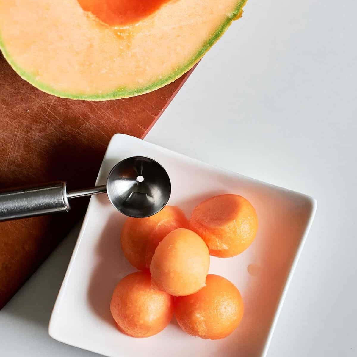 Small balls of cantaloupe in a square white dish.